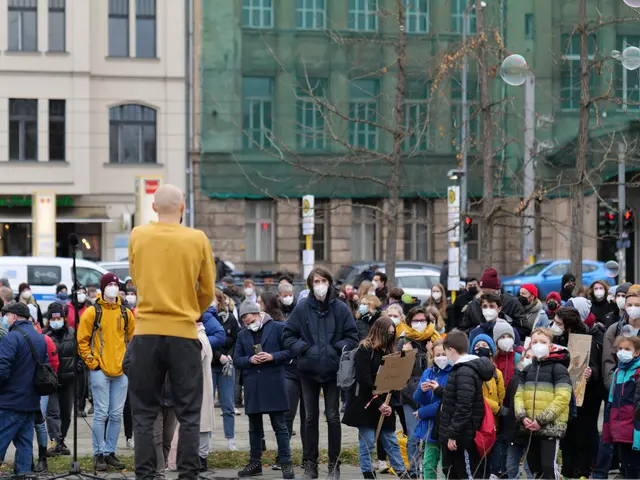 The image shows a group of people standing in front of a crowd of people, some of whom are holding...
