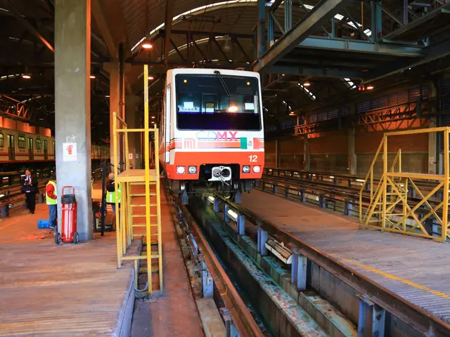The image shows a train traveling down train tracks next to a platform, with a group of people...