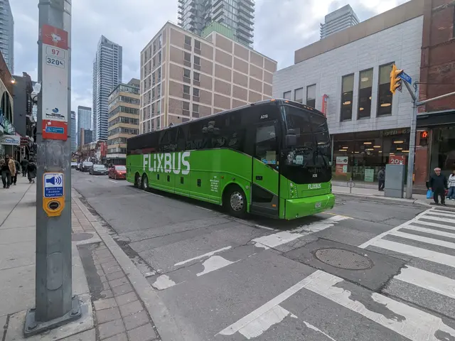 The image shows a green bus driving down a city street lined with tall buildings. On the left side...
