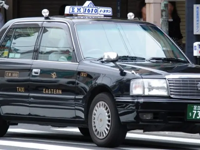 The image shows a black taxi cab driving down the street, with a person riding a bicycle in the...