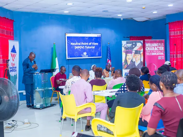 The image shows a man standing at a podium in front of a crowd of people sitting in chairs. He is...