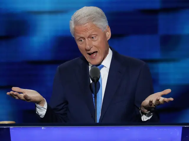 The image shows former President Bill Clinton standing in front of a podium with a microphone,...