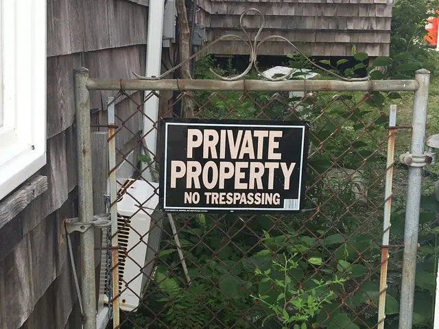 The image shows a private property sign on a chain link fence in front of a house, with a window on...