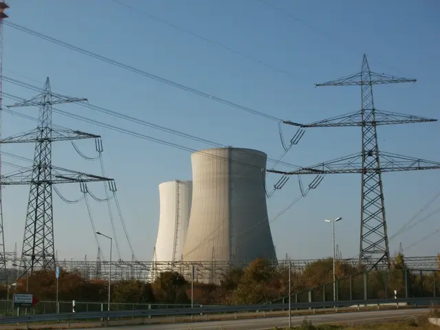 The image shows a nuclear power plant with power lines in front of it, surrounded by towers,...