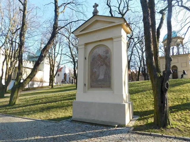 The image shows a monument in the middle of a park with a cross on it, surrounded by grass and...