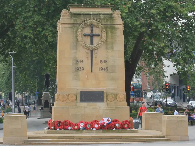 The image shows a war memorial in the middle of a city street, surrounded by wreaths on the ground....