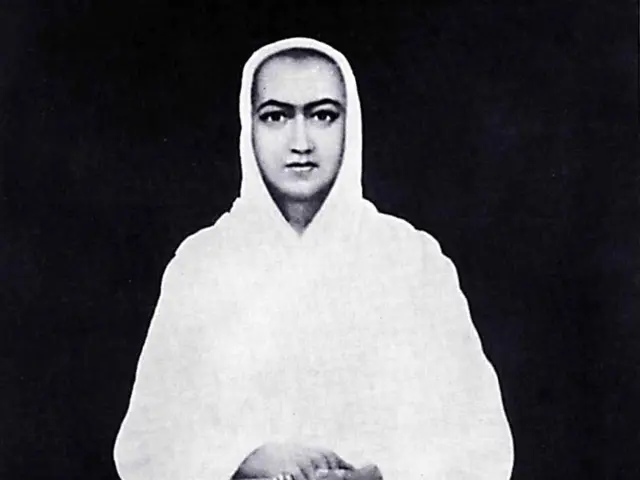 The image shows a black and white photo of a woman sitting in a lotus position on a platform, with...