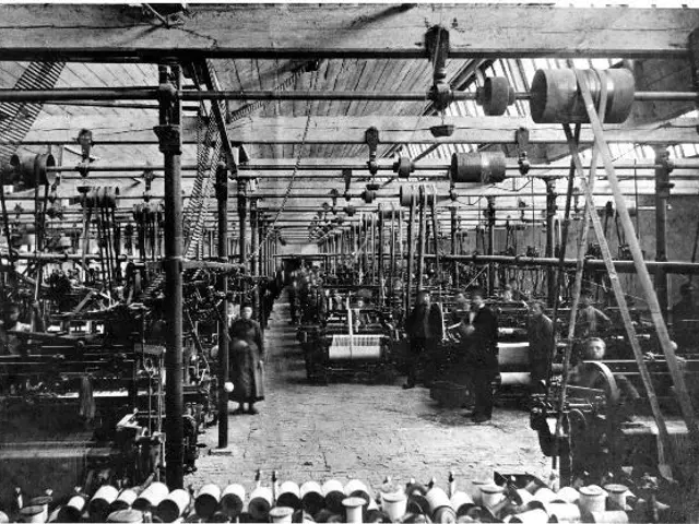 The image shows a black and white photo of people working in a factory, with machines, poles, and...