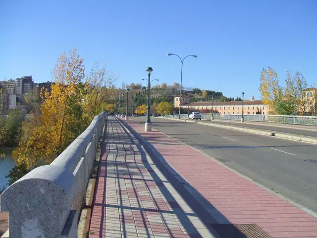 The image shows a pedestrian bridge over a river with cars driving on it. On either side of the...