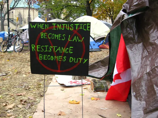 The image shows a tent with a sign that reads "When injustice becomes law, resistance becomes duty"...