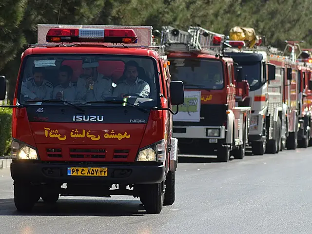 The image shows a line of fire trucks driving down a street, with people sitting in the vehicles....