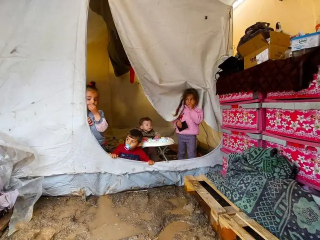 The image shows a group of children sitting inside of a tent in a Syrian refugee camp. On the right...