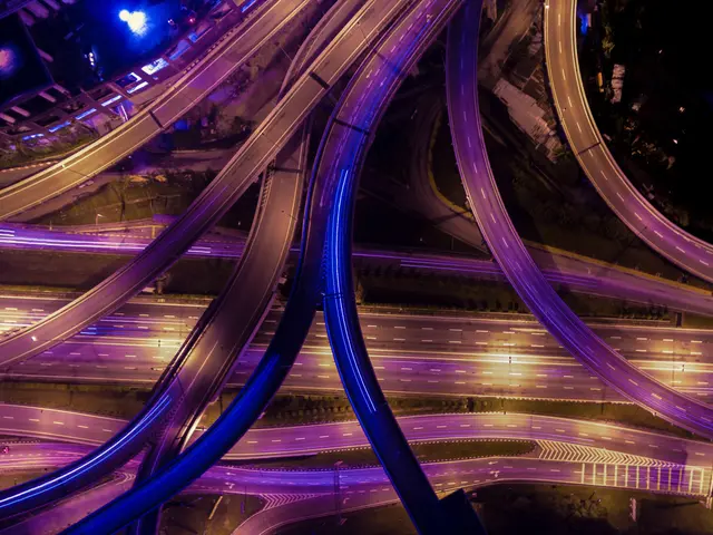 The image shows an aerial view of a highway intersection at night, with multiple lanes of traffic...