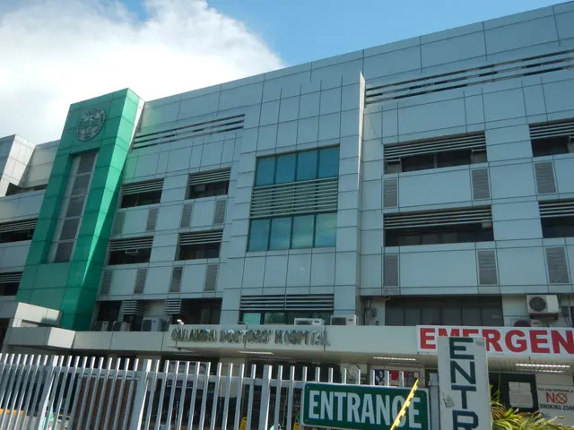 The image shows a large hospital building with a sign that reads "Emergency" in front of it,...