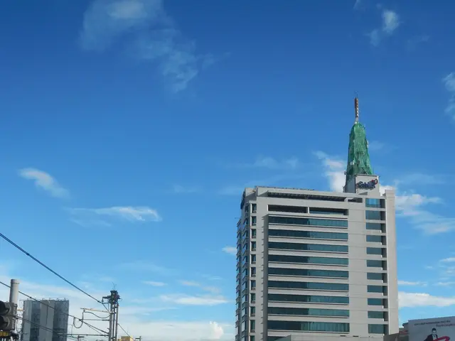 The image shows a city street filled with lots of traffic next to tall buildings, with a bridge on...