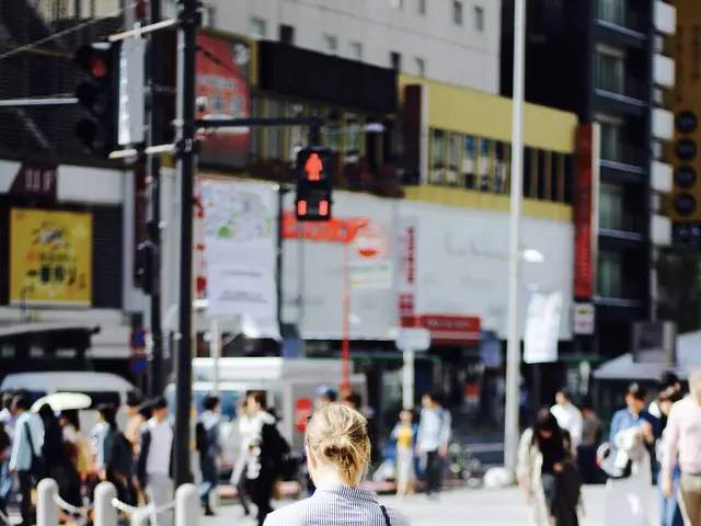 The image shows a woman crossing the street at a crosswalk, surrounded by a group of people,...
