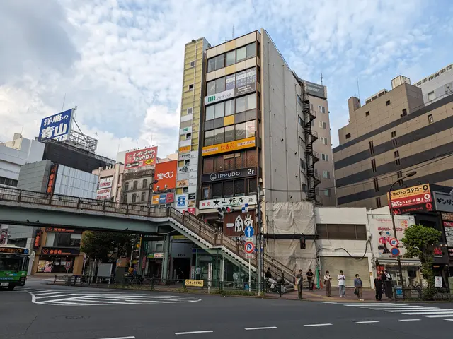 The image shows a bustling city street with a bus driving down it, surrounded by tall buildings...