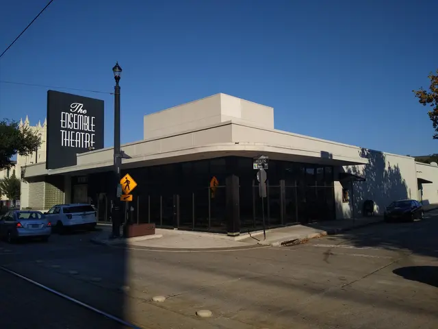 The image shows the Ensemble Theatre in Austin, Texas, with a few vehicles on the road in front of...