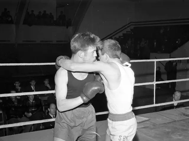 The image shows two boxers fighting in a boxing ring, surrounded by a group of people sitting in...