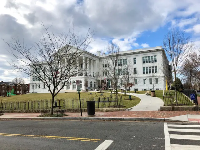 The image shows a large white building with a lot of windows on the side of it, surrounded by a...