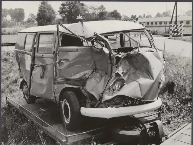 The image shows a black and white photo of a car that has been involved in a crash on a flatbed...