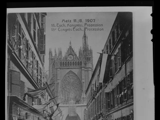The image shows a black and white photo of a crowd of people walking down a street in front of a...