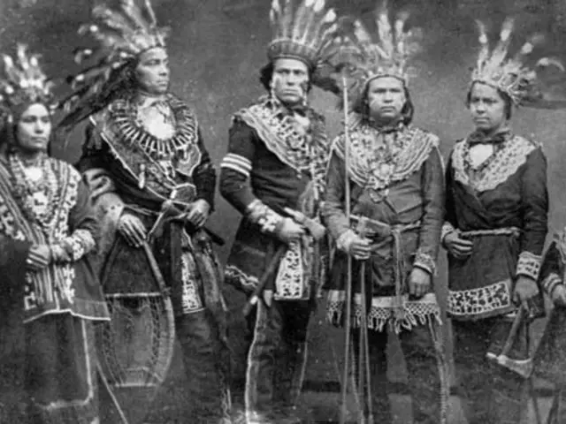 The image shows a group of Native American Indians standing next to each other, wearing traditional...