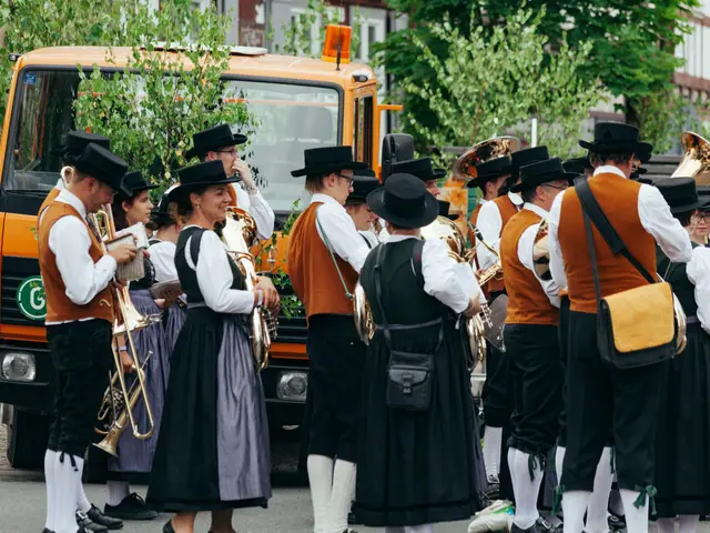 The image shows a group of people in traditional Bavarian clothing marching down the street,...