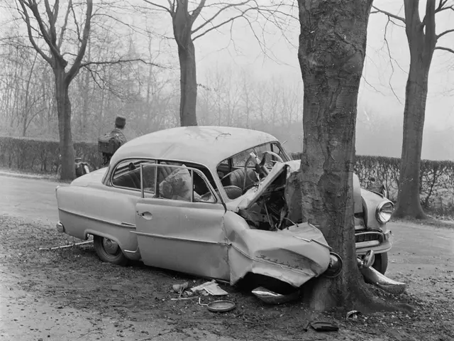 The image shows a black and white photo of a car that has crashed into a tree on the side of the...