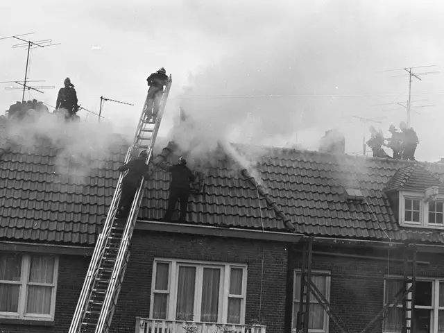 The image shows a group of firefighters on the roof of a house, with ladders, windows, railings,...