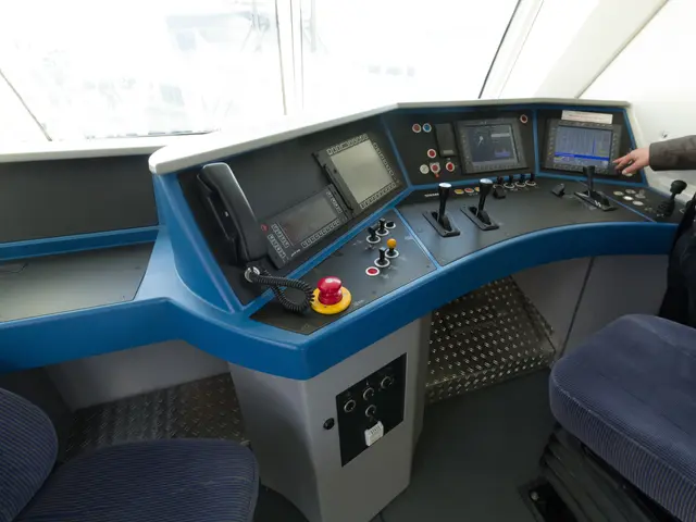 The image shows a man sitting at the control panel of a train, with two chairs in front of him and...
