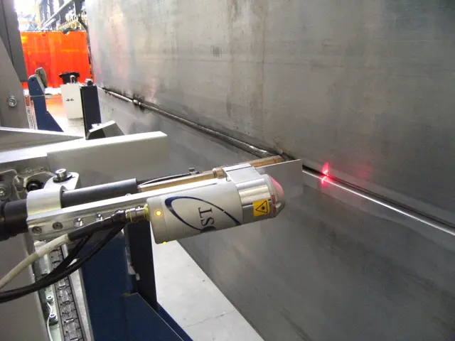 The image shows a laser cutting machine in a factory, with a wall on the right side and a few...